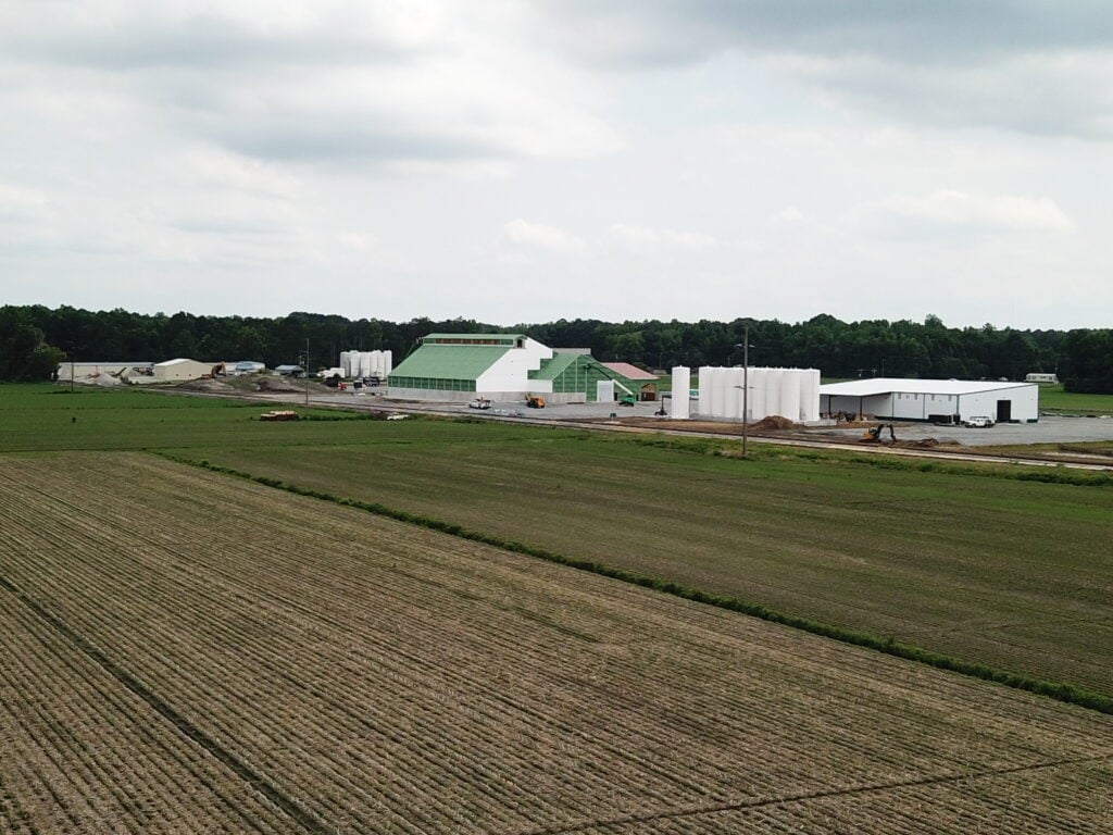 Nutrien dry Fertilizer blending and storage building being constructed by Stueve Construction with corn planted in the field and liquid fertilizer tanks